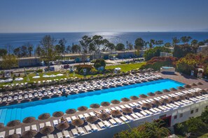 A large swimming pool with sun loungers and umbrellas, surrounded by greenery and buildings, with a view of the sea. - Hotel SU & Aqualand (Antalya)