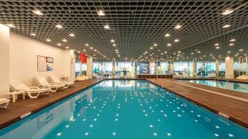 Piscina interna com espreguiçadeiras e teto com padrão de grade.