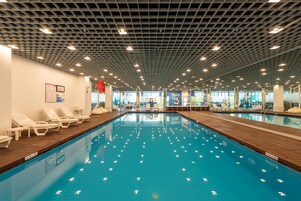 Piscina interna com espreguiçadeiras e teto com padrão de grade.
