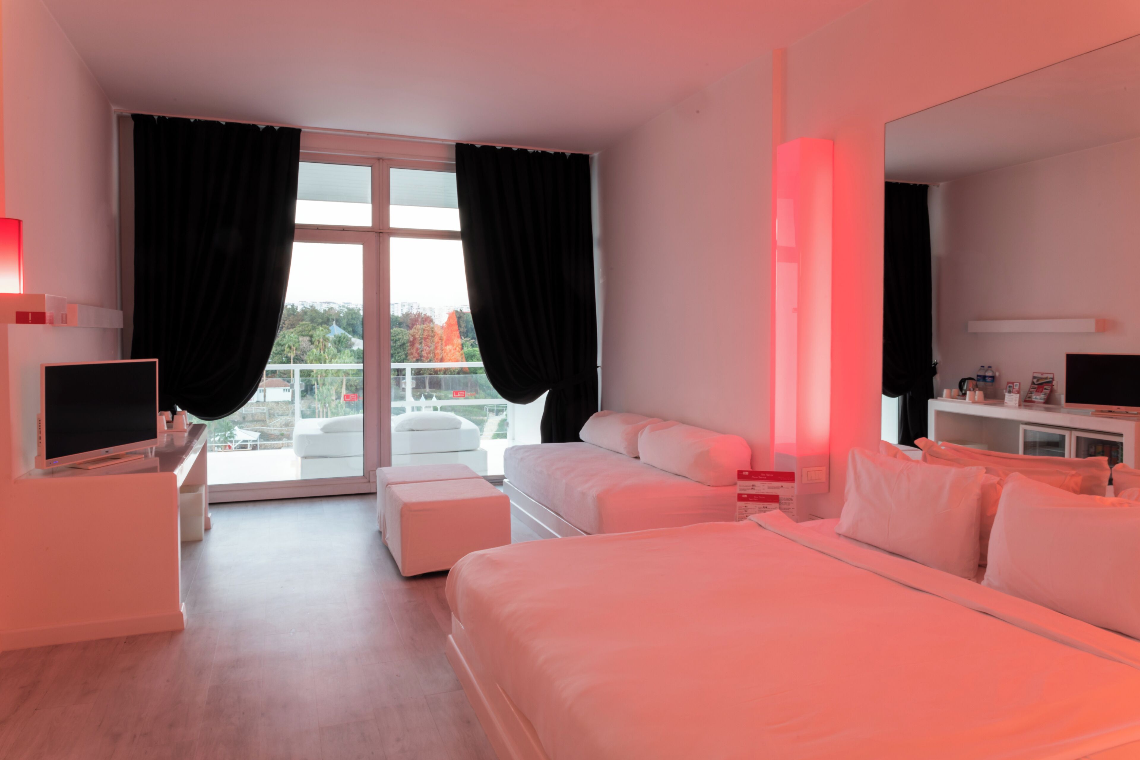 A modern hotel room with a large bed, a sofa, a TV, and a balcony with curtains.