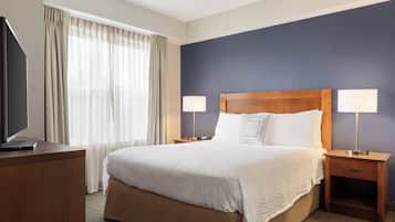 A hotel room with a large bed, two bedside tables with lamps, a TV on a wooden desk, and a window with curtains.