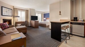 Habitació d'hotel amb zona saló, un llit, escriptori, televisió, llar de foc i cuineta.