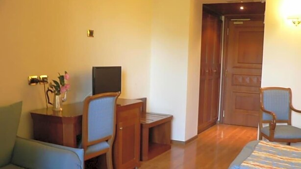 Une chambre d’hôtel avec un lit, un bureau et une chaise, une télévision et une petite table agrémentée de fleurs.