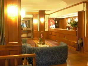 A hotel lobby with a reception desk, seating area, and a staircase.