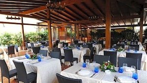 Un espace de restauration en plein air, avec des tables disposées pour quatre personnes, recouvert d’une pergola en bois et entouré de chaises et de plantes.