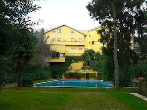 A yellow building with a swimming pool surrounded by greenery.