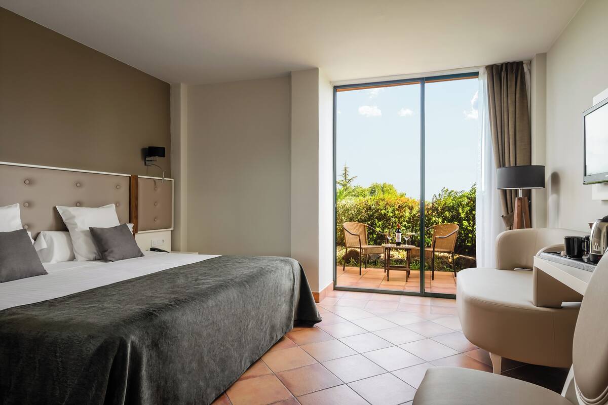 A hotel room with a bed, a desk, a chair, and a view of the outdoors.