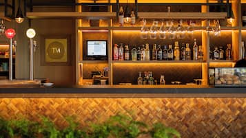 Zona de bar con estantes llenos de botellas, una pantalla de televisión y copas colgantes.