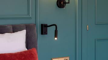 A hotel room with teal walls, a bed with white and red bedding, a black nightstand, and a wall-mounted light fixture.