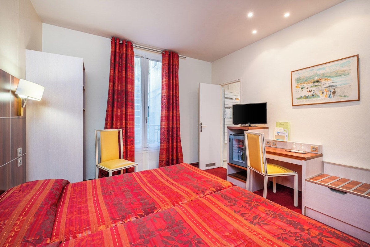 A hotel room with a bed, a desk, a chair, a television, and a painting on the wall.