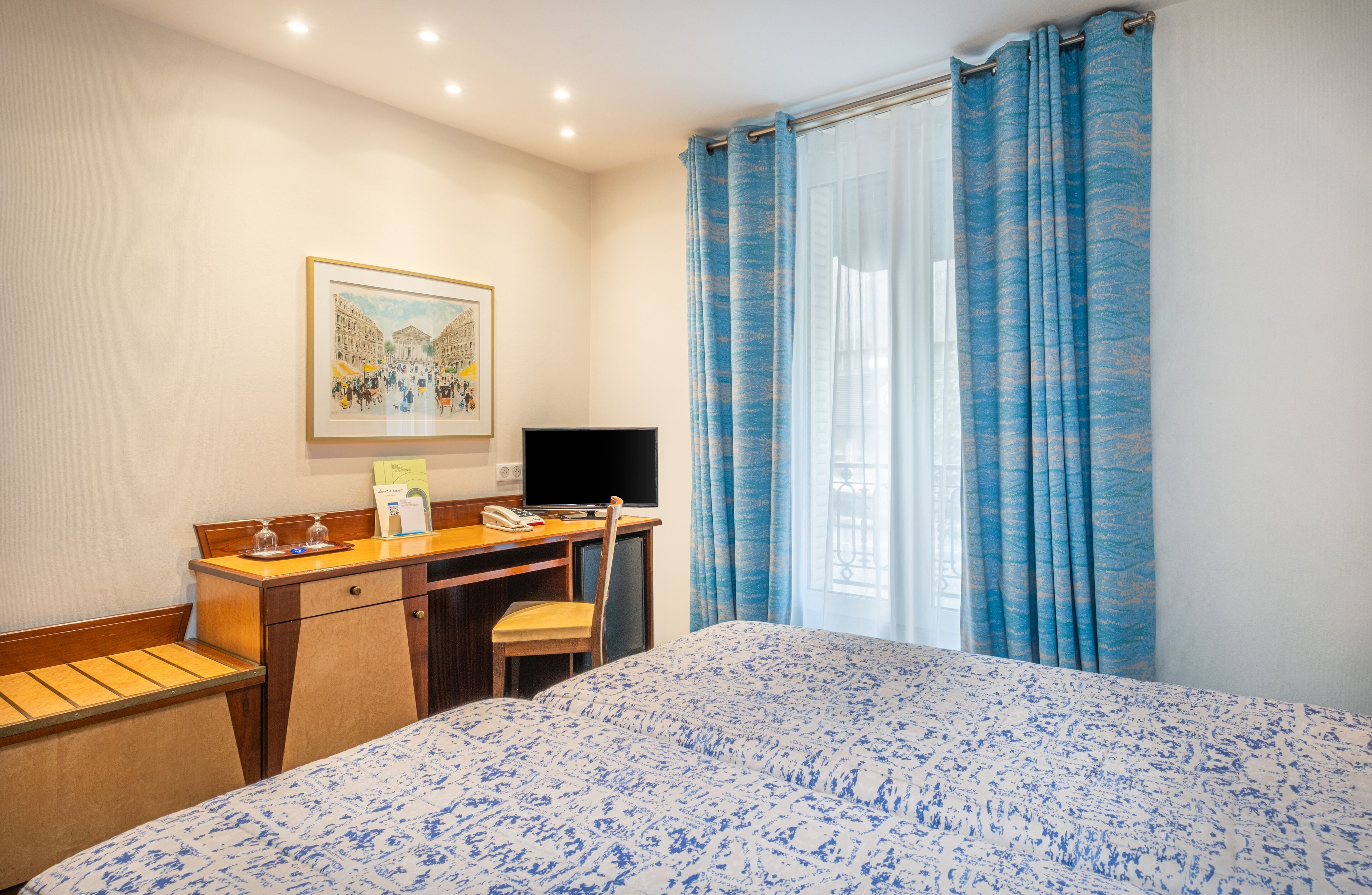 A hotel room with a bed, a desk with a computer, a chair, and a framed picture on the wall.