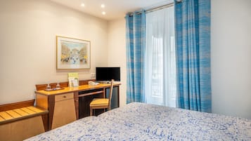 A hotel room with a bed, a desk with a computer, a chair, and a framed picture on the wall.