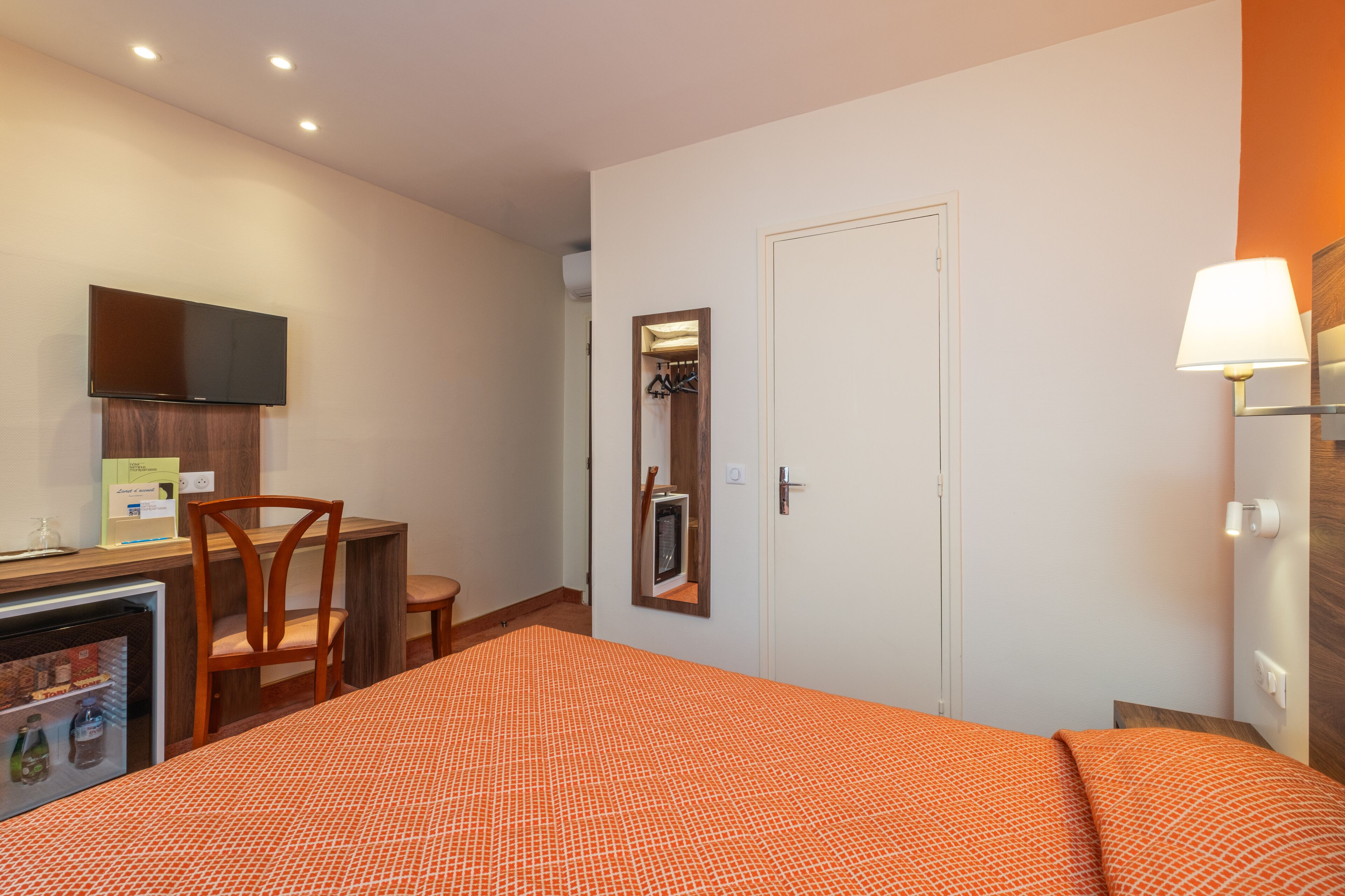 Ein Hotelzimmer mit einem Bett, einem Schreibtisch mit Stuhl, einem Fernseher, einem Spiegel und einer Lampe.