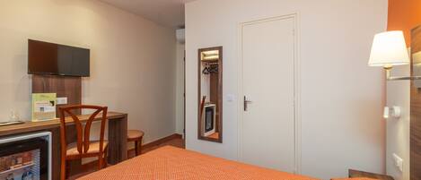 Ein Hotelzimmer mit einem Bett, einem Schreibtisch mit Stuhl, einem Fernseher, einem Spiegel und einer Lampe.