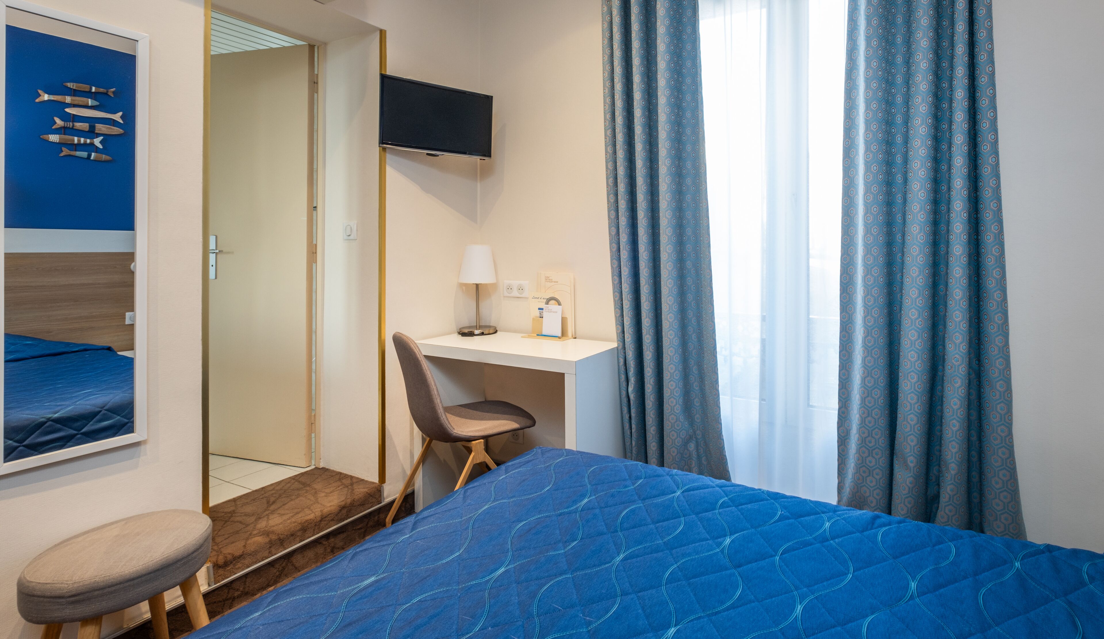 Habitación de hotel con cama, escritorio con silla, televisor y ventana con cortinas.
