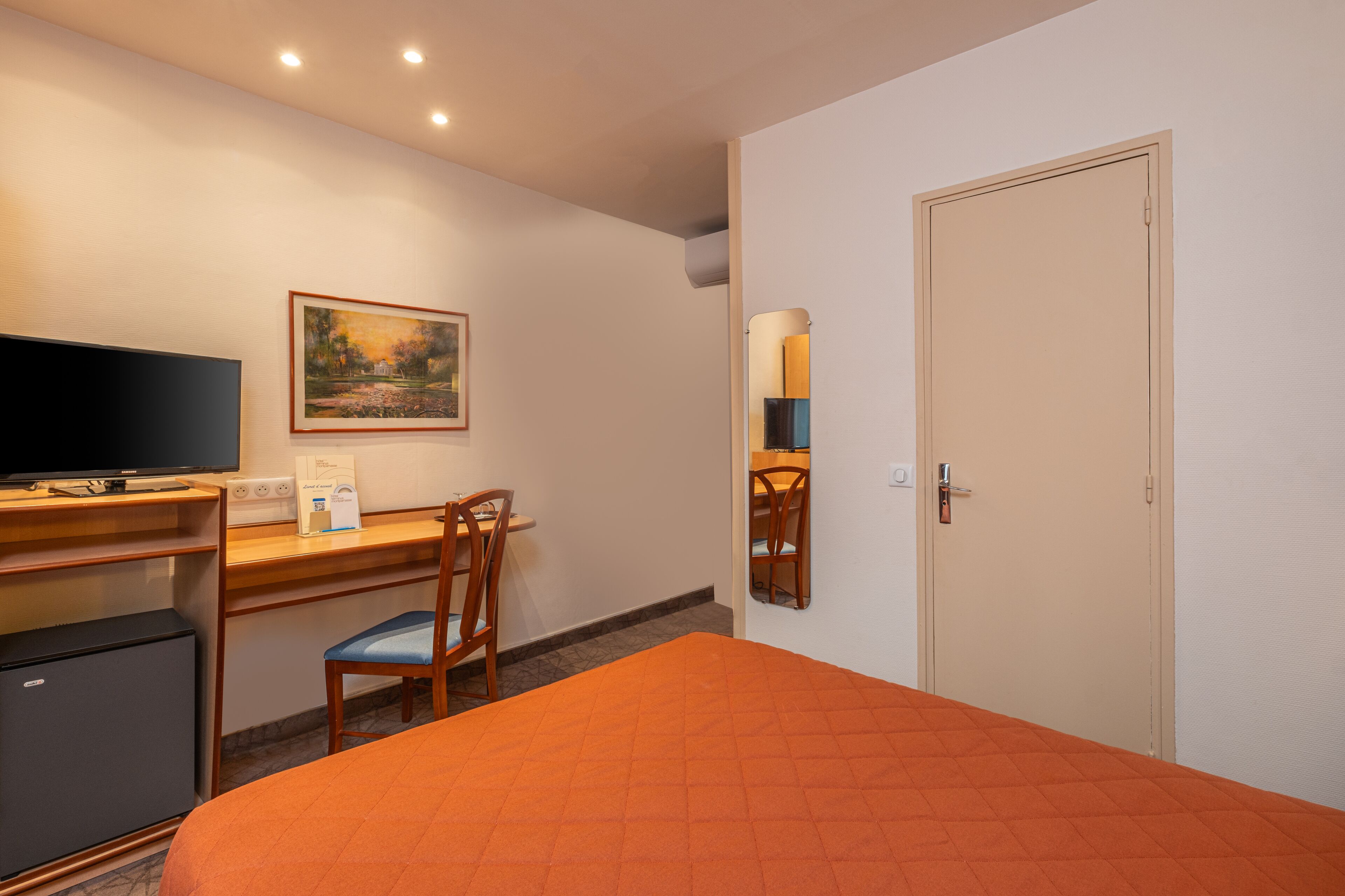 Une chambre d’hôtel avec un lit, un bureau avec un ordinateur, une chaise, une télévision et une porte.