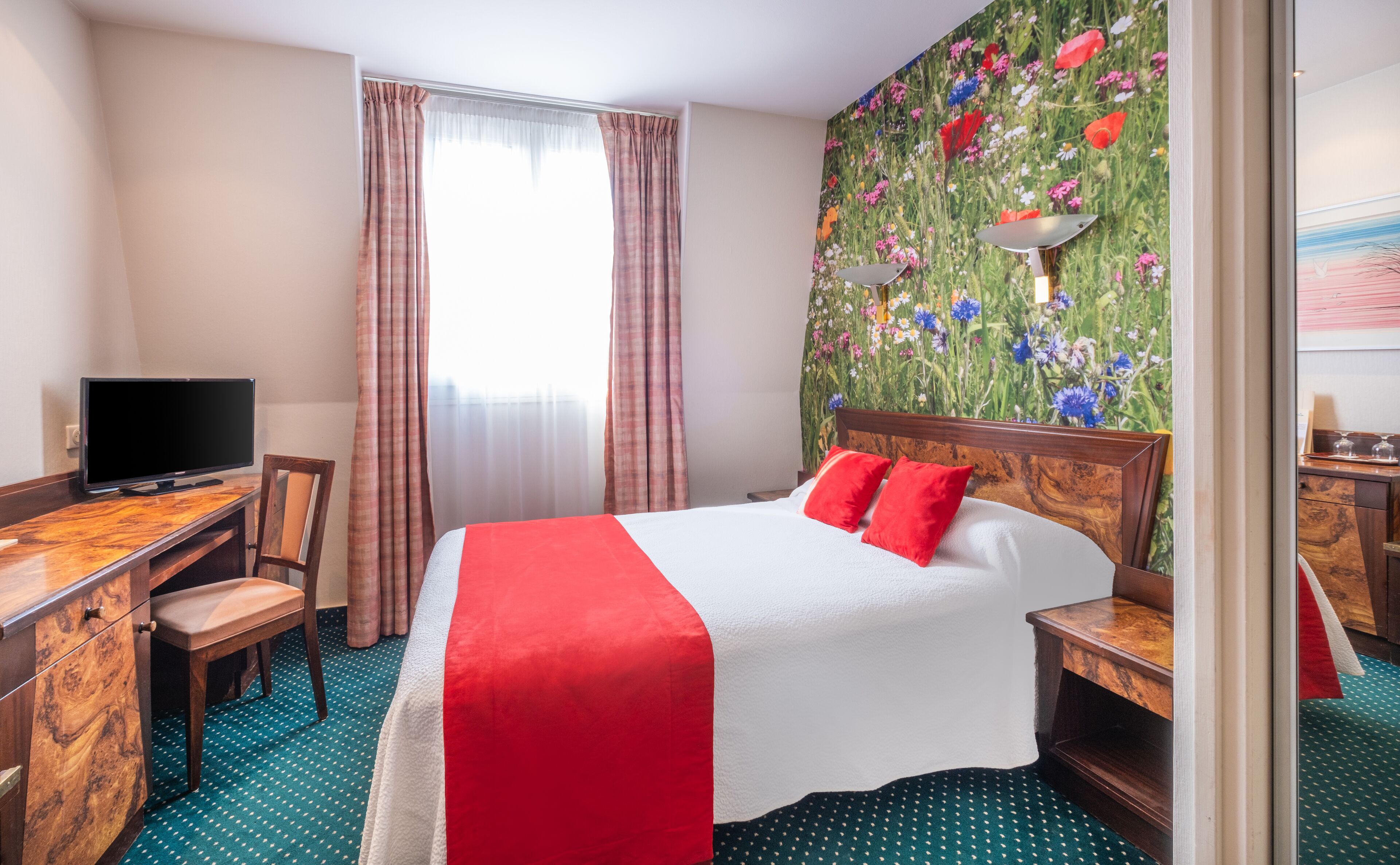 A hotel room with a bed, a desk, a chair, a television, and a window with curtains.