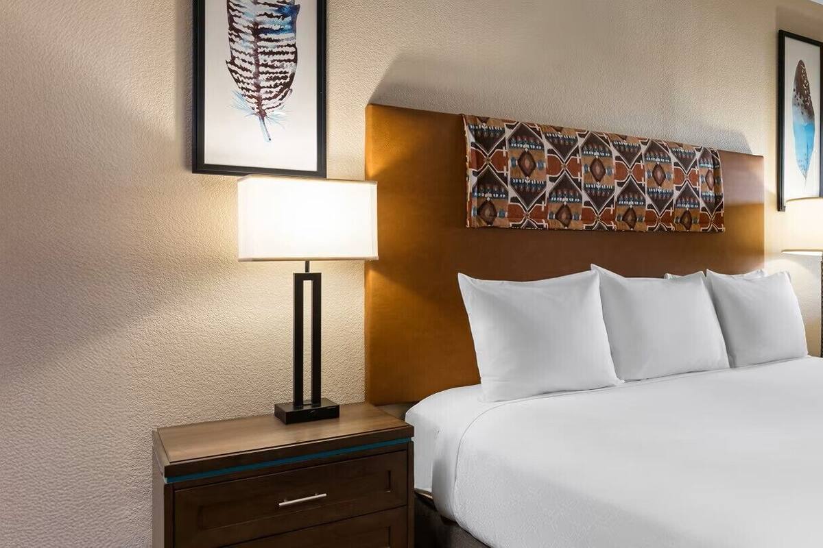 A hotel room with a large bed, two bedside tables with lamps, a wall-mounted artwork, and a window with blinds.