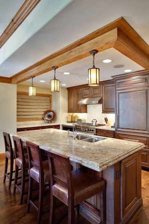 A kitchen with a large island, wooden cabinets, and pendant lighting.