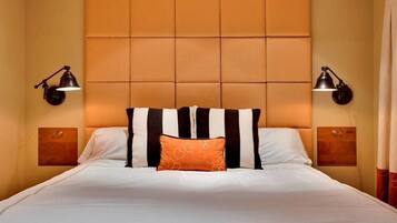 Una habitación de hotel con una cama grande, cabecera acolchada, dos lámparas de noche y una pequeña obra de arte sobre la mesita.