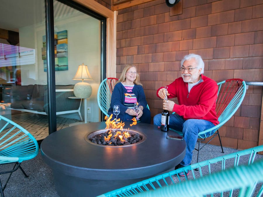 A man and a woman sitting at a round table with a fire pit in the center, surrounded by turquoise chairs.