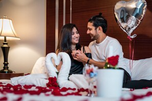 Una coppia seduta su un letto, con petali di rosa, un palloncino a forma di cuore e un vaso di fiori.