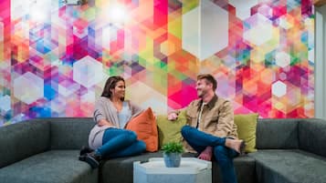 Two people sitting on a grey sofa with a colorful geometric wall behind them.
