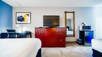 Una habitación de hotel con cama, escritorio, cómoda, televisor, espejo y microondas.