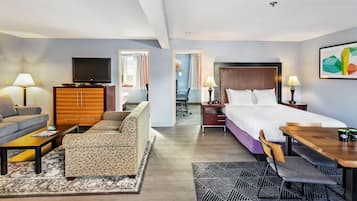 A hotel room with a sofa, a bed, a desk, a TV, and a dining area.