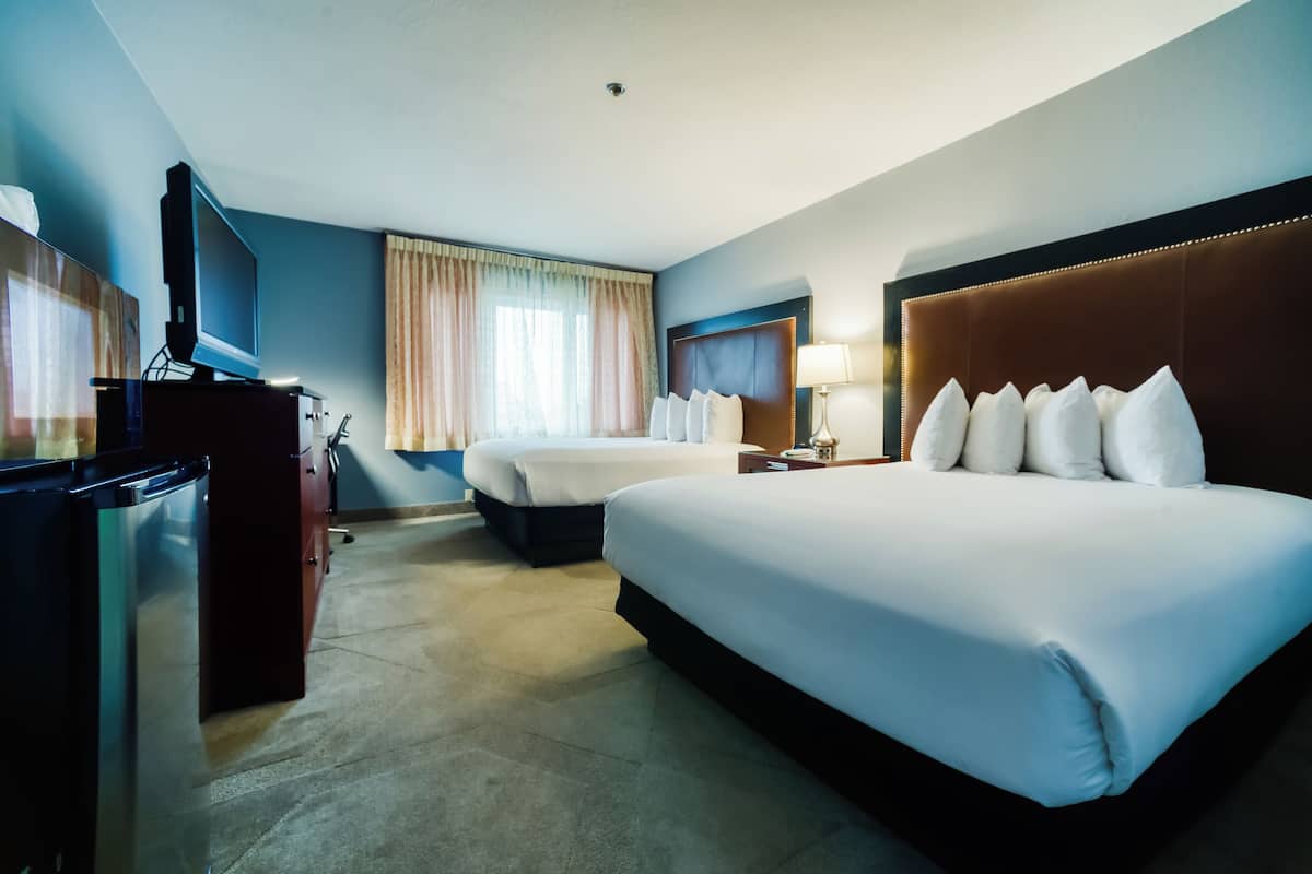 A hotel room with two beds, a desk with a television, and a window with curtains.