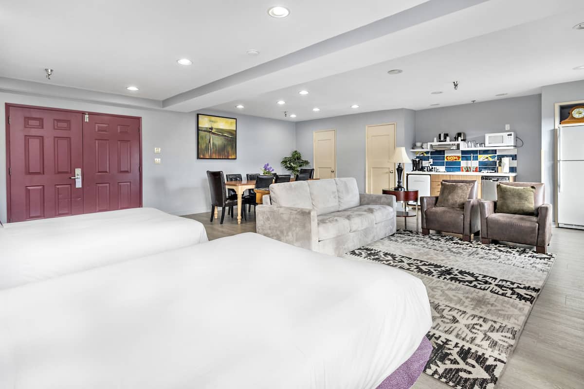 A hotel room with two beds, a sofa, a dining area, and a kitchenette.