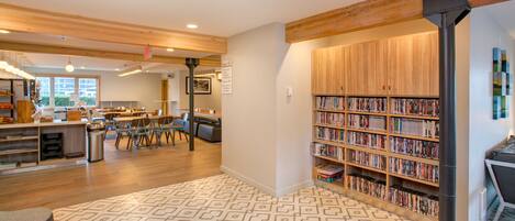 A library with wooden bookshelves, a patterned carpet, and a dining area with tables and chairs.