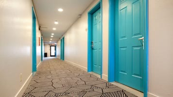 A hallway with teal doors, patterned carpet, and recessed lighting.