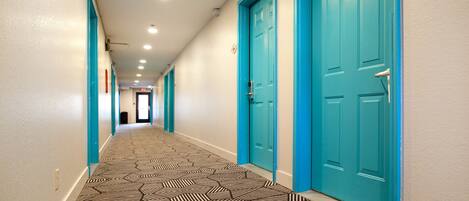 A hallway with teal doors, patterned carpet, and recessed lighting.