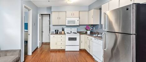A modern kitchen with white cabinets, a stainless steel refrigerator, a microwave, and a stove.