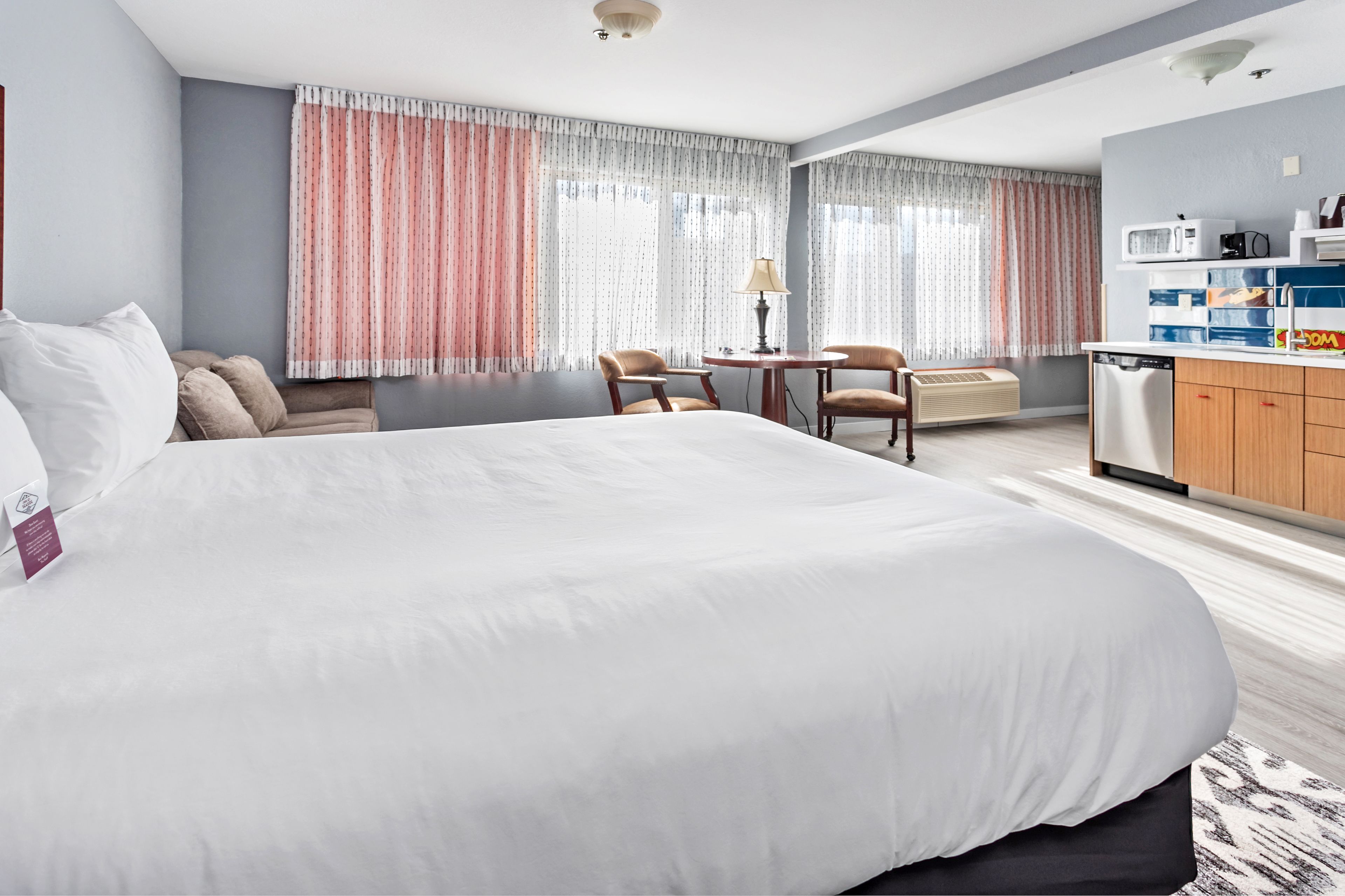 A hotel room with a large bed, a desk with two chairs, a microwave, and a small kitchenette.