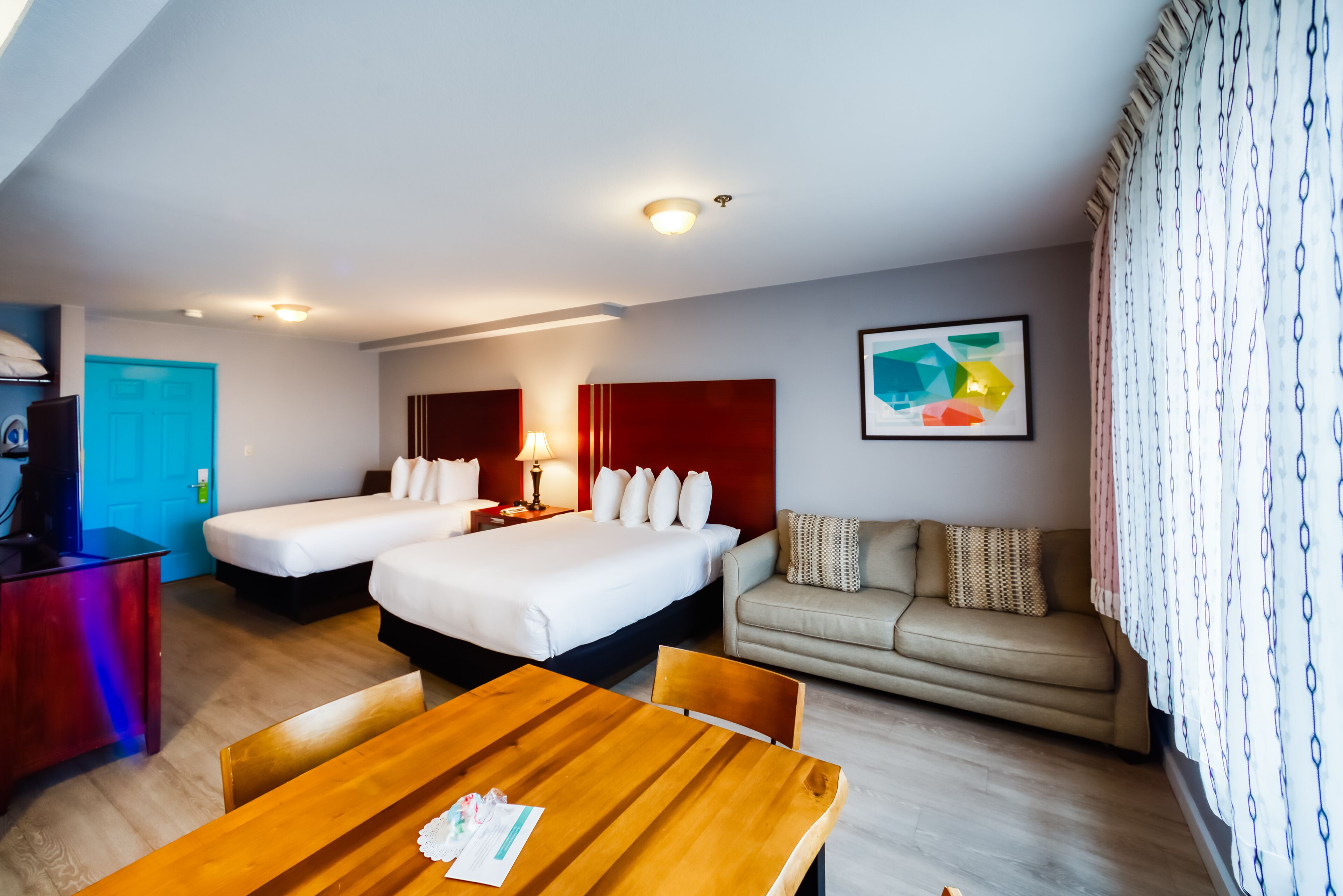 A hotel room with two beds, a sofa, a wooden table, and a TV.