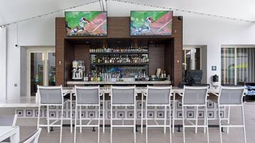 A bar area with a long counter, multiple chairs, and a wall-mounted TV screen displaying a baseball game.
