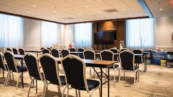 A conference room with multiple tables and chairs, a large flat-screen TV, and a view of the outdoors through large windows.