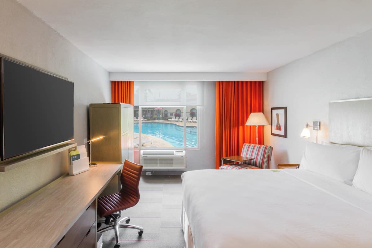 Une chambre d’hôtel équipée d’un lit, d’un bureau, d’une chaise et offrant une vue sur une piscine.