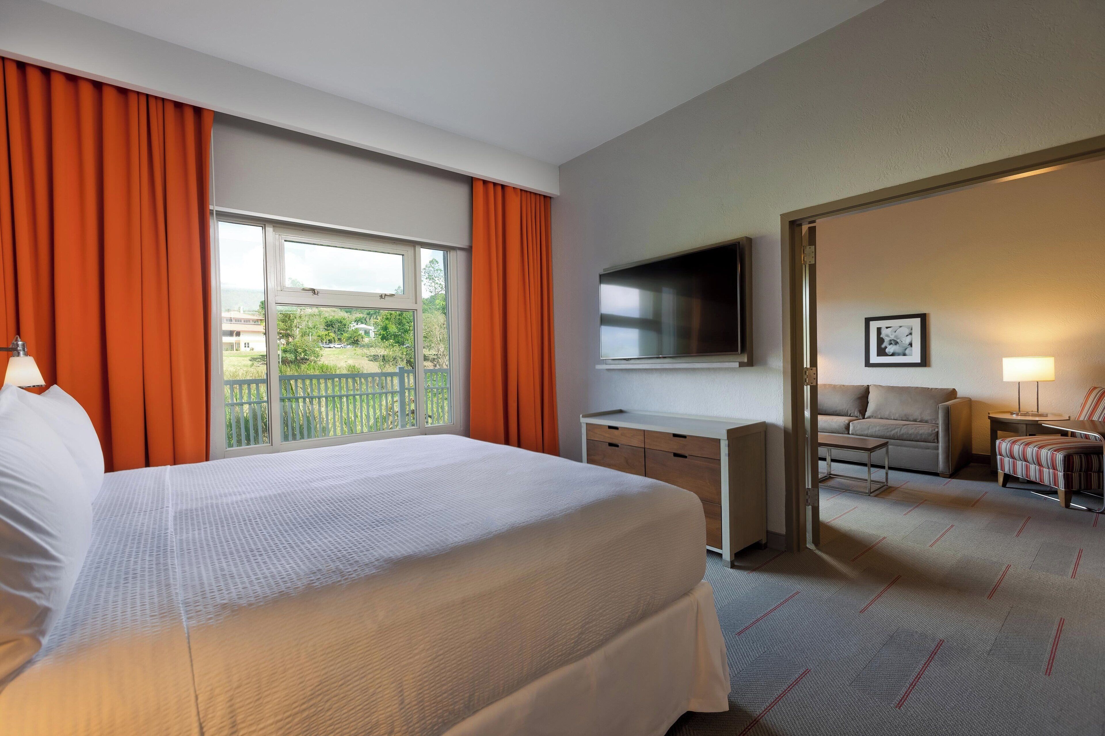 Ein Hotelzimmer mit einem großen Bett, einem Schreibtisch, einem Fernseher, einem Sofa und einem Sessel.