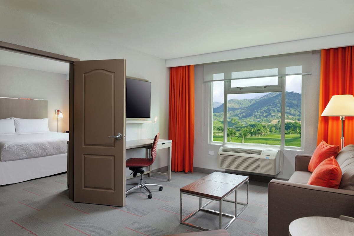 Une chambre d’hôtel avec un lit, un bureau, une chaise et une vue sur les montagnes par la fenêtre.