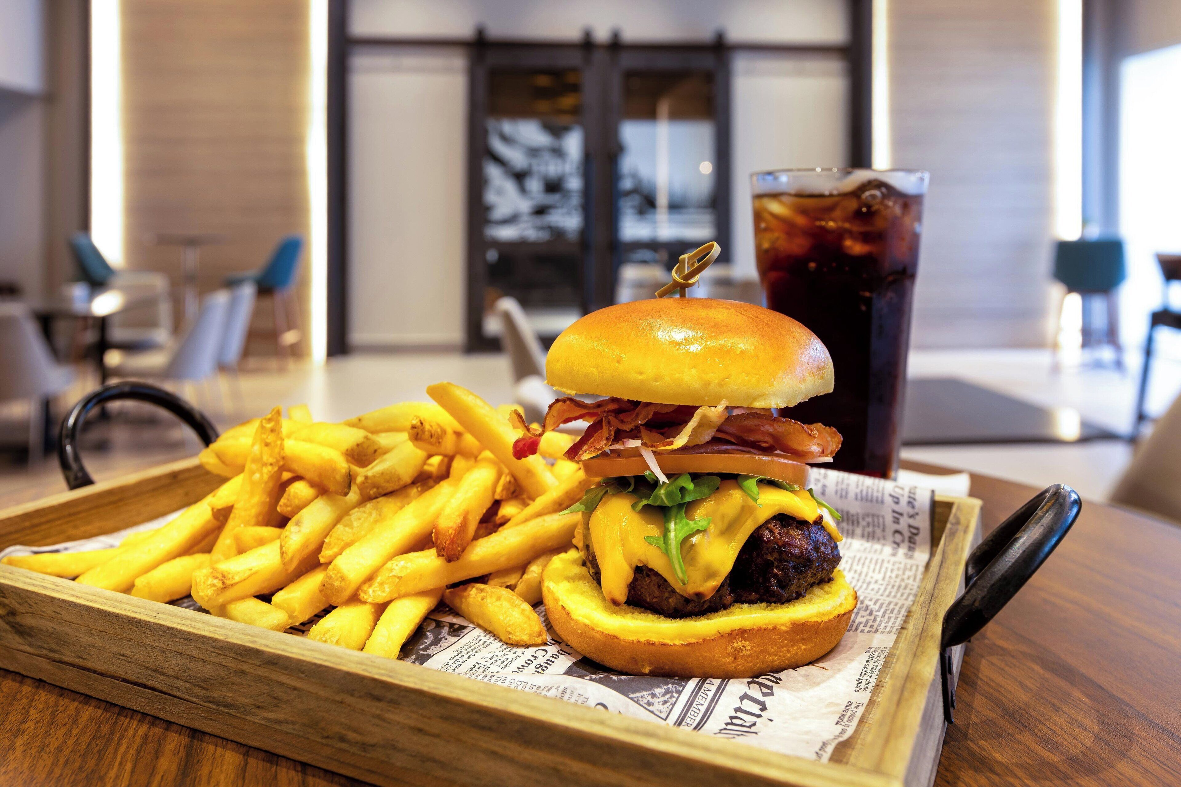 Een dienblad met een hamburger, friet en een drankje op een houten tafel.