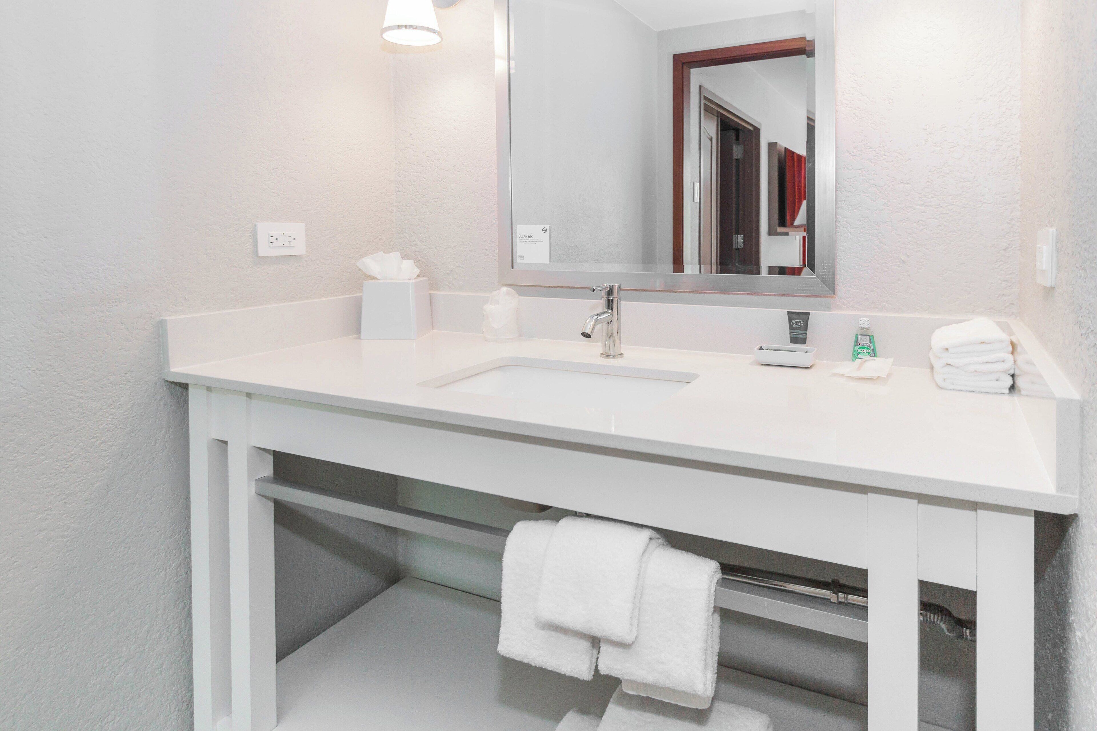 A white bathroom with a sink, mirror, and towel rack.