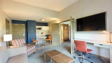 A modern hotel room with a living area, kitchenette, and a large TV.