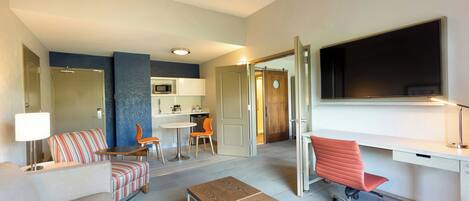 Habitación de hotel moderna con sala de estar, kitchenette y un televisor grande.