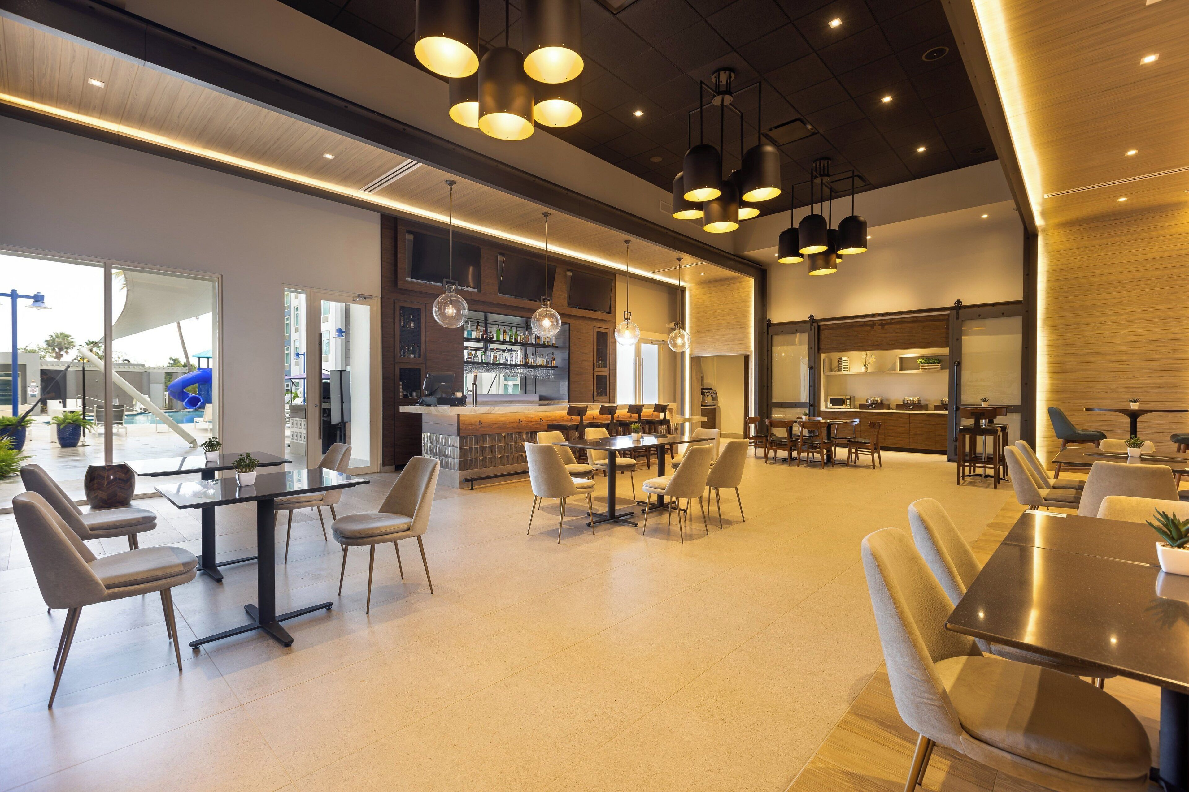 A modern hotel lobby with a bar area, seating arrangements, and a view of the outside.