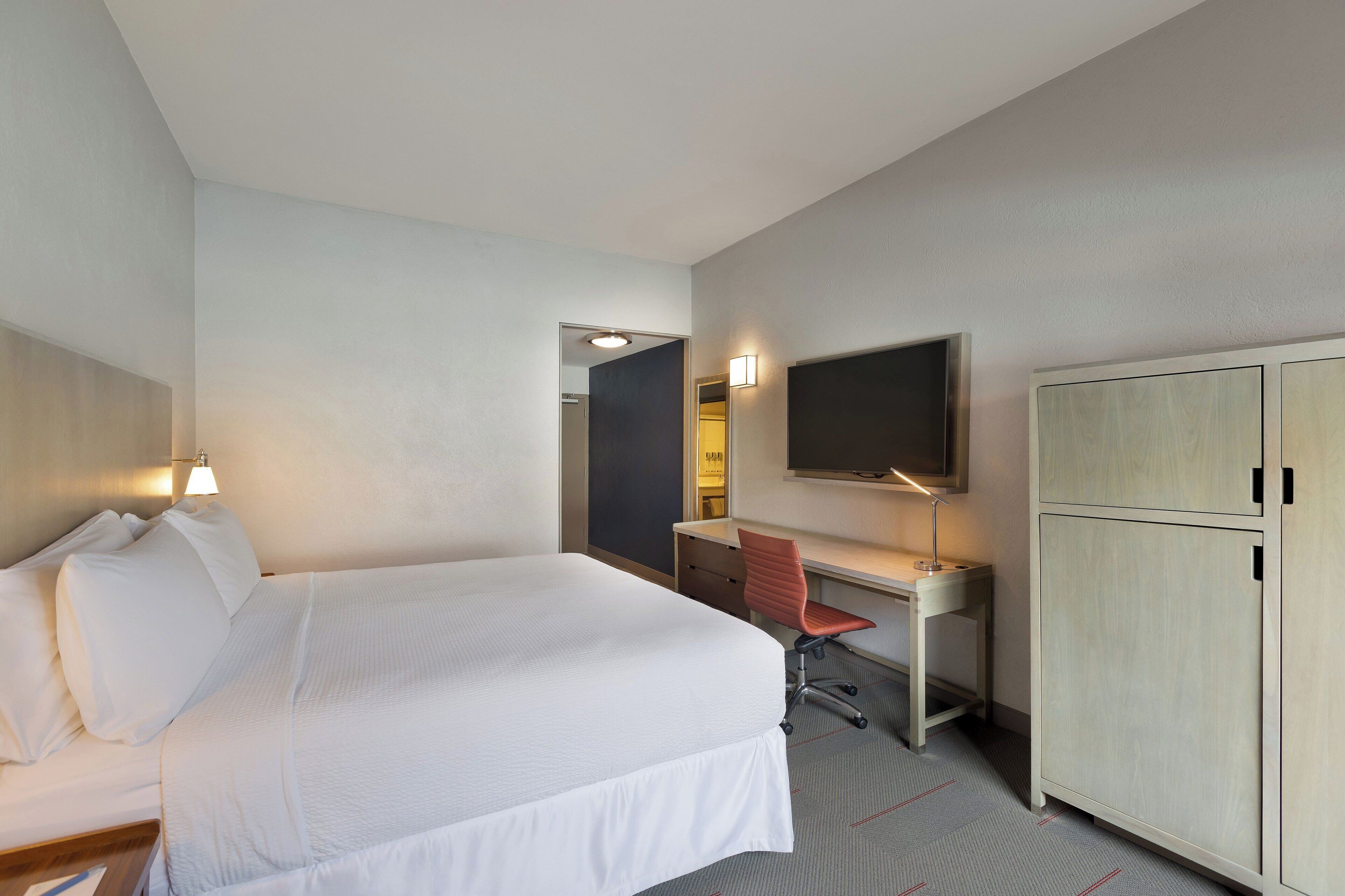 A hotel room with a large bed, a desk with a chair, a television, and a wardrobe.