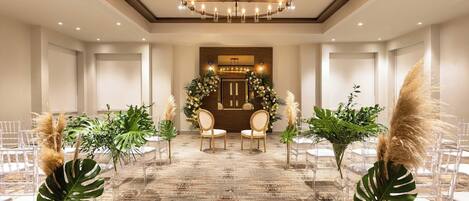 A spacious hall with a patterned carpet, clear chairs, and a chandelier.