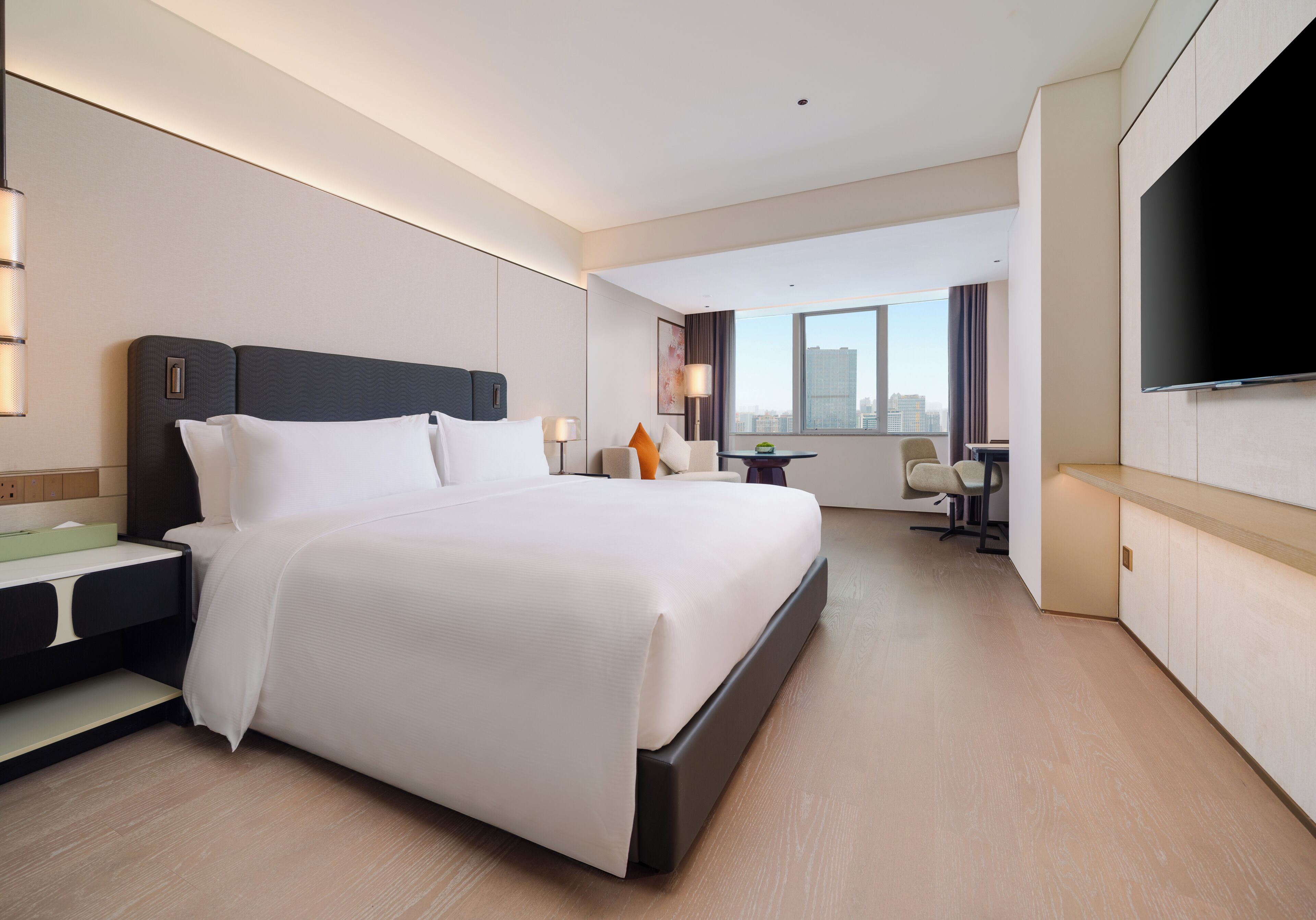 Una habitación de hotel moderna con una cama grande, un escritorio, un televisor de pantalla plana y vistas a la ciudad.